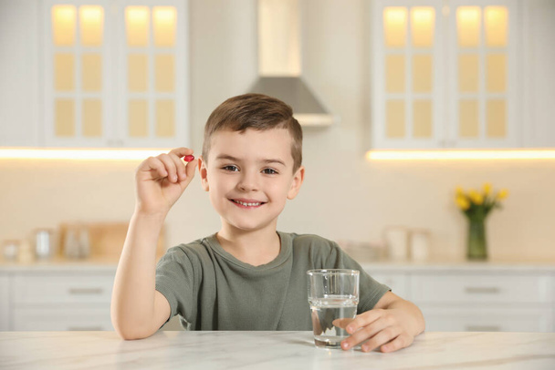Kleiner Junge mit Glas Wasser und Vitaminkapsel in der Küche - Foto, Bild