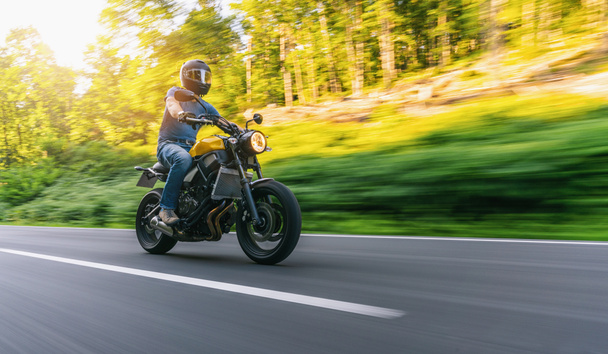 motocykl na leśnej drodze jadący o zachodzie słońca. zabawy jazdy pustą drogą na wycieczkę motocyklową. copyspace dla Twojego indywidualnego tekstu. - Zdjęcie, obraz