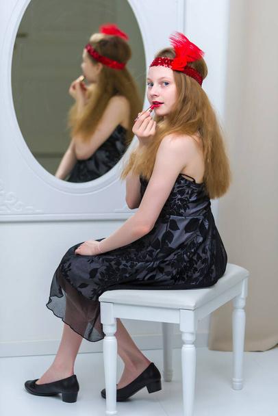 Beautiful girl of school age paints lips with lipstick and looks in the mirror. - Foto, Bild