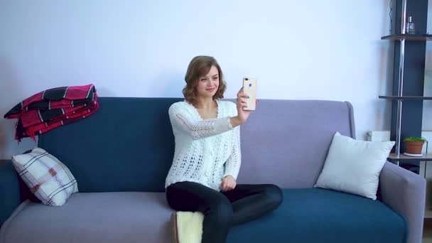 The girl sits on the couch and communicates via video. - Filmagem, Vídeo