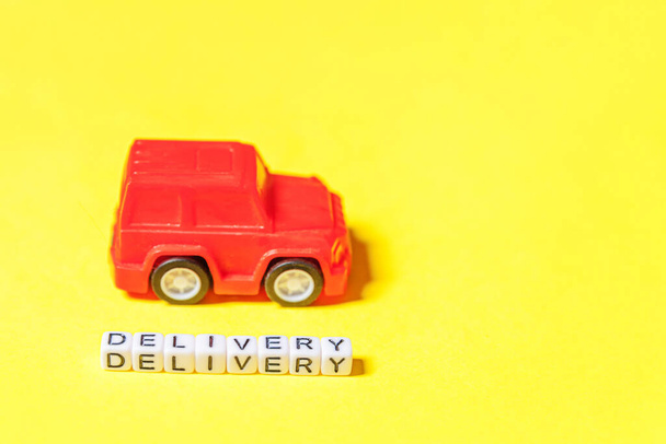 Ontwerp eenvoudig rode speelgoedauto en opschrift DELIVERY woord geïsoleerd op gele kleurrijke achtergrond. Internet winkelen online aankoop e-commerce pakketten bezorgservice concept. Kopieerruimte - Foto, afbeelding