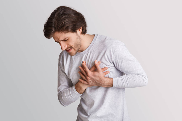 Ataque cardíaco a temprana edad. El hombre presiona sus manos para el pecho y el dolor de expresión facial
 - Foto, imagen