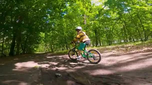 A boy rides a bicycle on a path in the forest. The road in the spring park. - Materiał filmowy, wideo