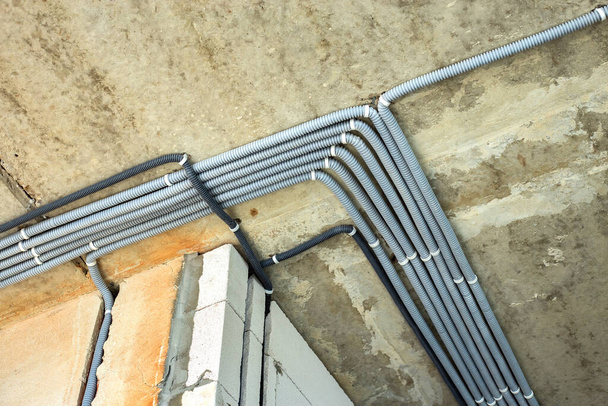 Ηλεκτρικά καλώδια τοποθετημένα σε προστατευτική γείωση τοποθετημένα στην οροφή και στον τοίχο σε χώρο υπό κατασκευαστικές εργασίες. - Φωτογραφία, εικόνα