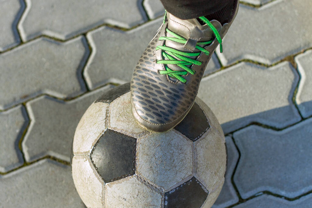 Close-up of boy foot in sport shoes on football ball outdoors on sunny pavement background. Vacations activity, sport and recreation concept. - Photo, Image