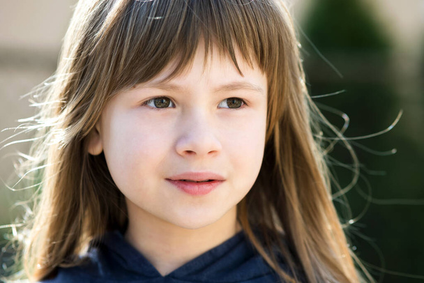 Portrait of pretty child girl with gray eyes and long fair hair outdoors on blurred bright background. Cute female kid on warm summer day outside. - Fotó, kép