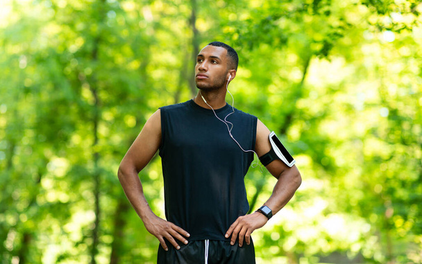 Schöner schwarzer Mann mit Kopfhörern, der während seines morgendlichen Laufs im Park Musik hört - Foto, Bild