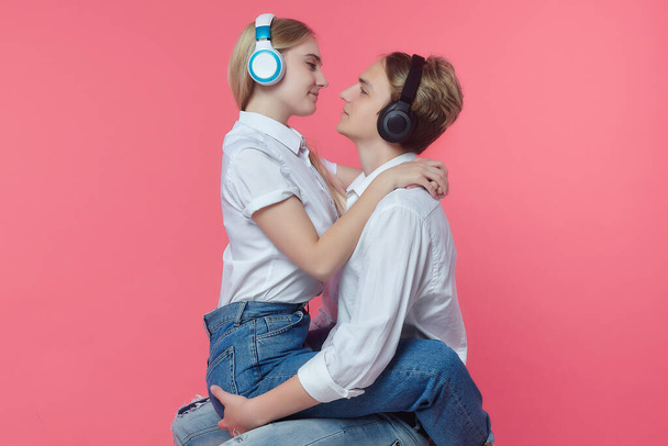 guy and girl in headphones. listen to music while expressing emotions with a kiss. pink back - Photo, image