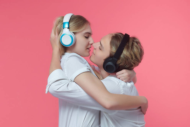 guy and girl in headphones. listen to music while expressing emotions with a kiss. pink back - Foto, Bild