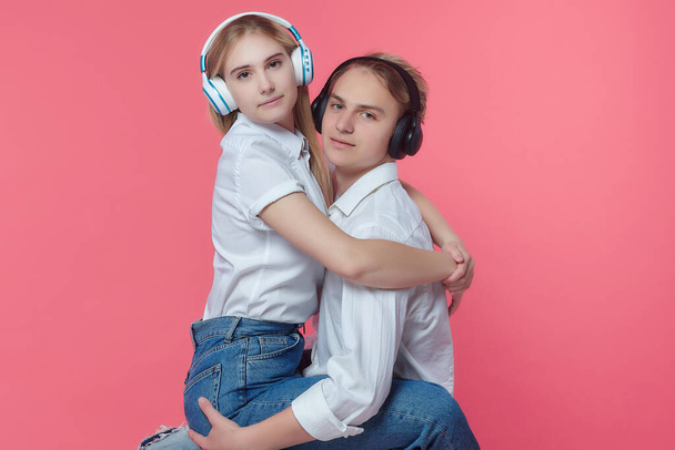 guy and girl in headphones. listen to music while expressing emotions with a kiss. pink back - Photo, Image