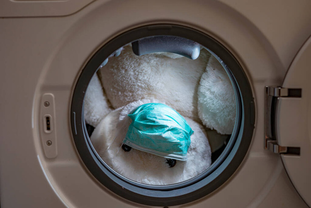 White bear puppy wearing green mask in washing machine - Foto, Imagen