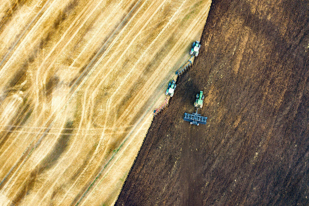 Вид с воздуха на трактор, вспахивающий черное сельскохозяйственное поле после уборки урожая поздней осенью. - Фото, изображение