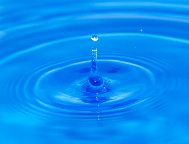 A drop of water falling in blue water - 写真・画像