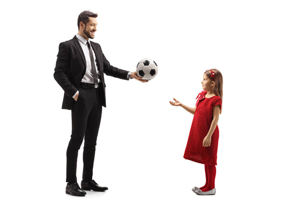 Ganztägige Profilaufnahme eines Mannes in einem Anzug, der einem kleinen Mädchen auf weißem Hintergrund einen Fußball gibt. - Foto, Bild