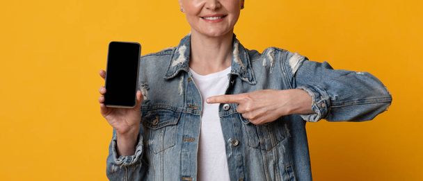 Smartphone-Attrappe. Lächelnde Frau mittleren Alters zeigt auf schwarzen leeren mobilen Bildschirm - Foto, Bild