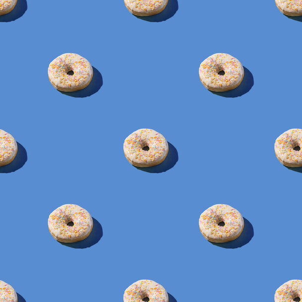 Vanilla white donuts with sprinkles, sweet glazed dessert seamless pattern on blue background - Photo, Image