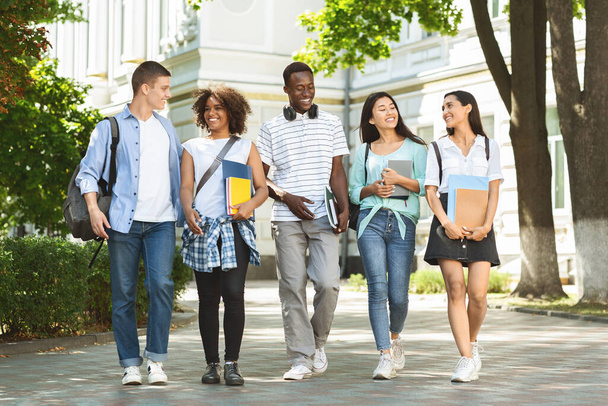 生徒のコミュニケーション。大学のキャンパスで屋外を歩く大学生の友人のグループ - 写真・画像