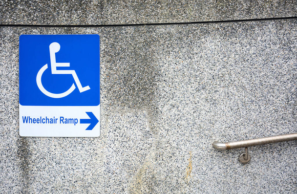 公共の場所に鋼の手すりと汚れた小石の石の壁のテクスチャで障害者のための車椅子のランプ記号、コピースペース - 写真・画像