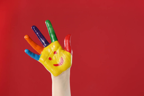 Kid with smiling face drawn on palm against red background, closeup. Space for text - Foto, Imagen