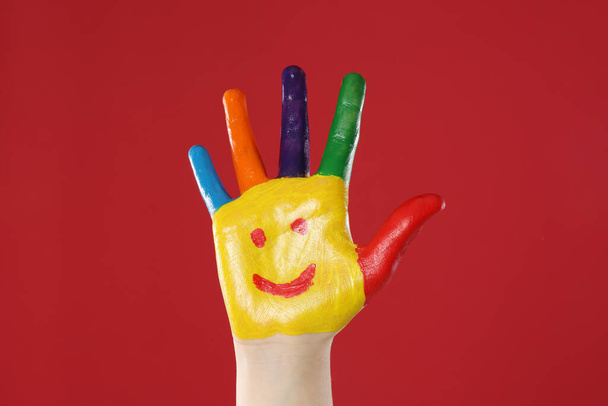 Kid with smiling face drawn on palm against red background, closeup - Fotó, kép