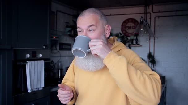 Šťastný dospělý vousatý muž pije kávu v dopoledních hodinách doma kuchyně a tance, dobré ráno koncepce, rozmazané pozadí - Záběry, video