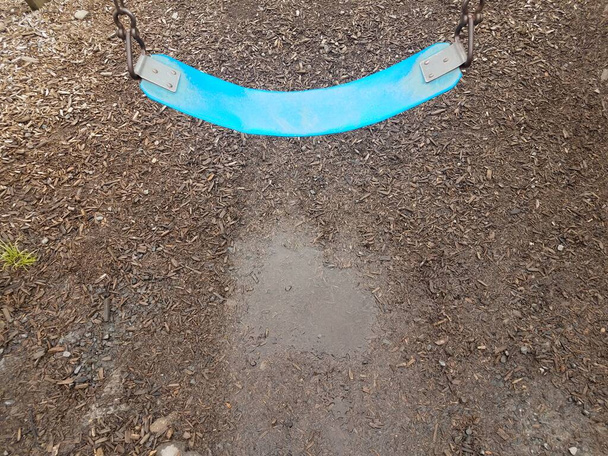 blue swing on playground with water puddle and wood chips or bark dust - Photo, Image