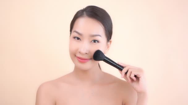 felvétel gyönyörű ázsiai nő tiszta bőr és smink ecset bézs háttér - Felvétel, videó