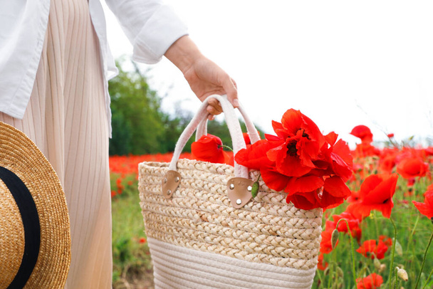 Woman holding handbag with poppy flowers in beautiful field, closeup - 写真・画像