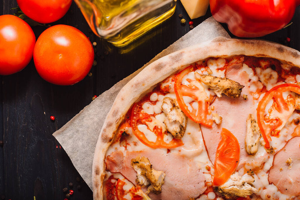 Sabrosa pizza italiana e ingredientes de cocina tomates, hierbas, queso sobre fondo de hormigón negro. Pizza de panceta caliente
. - Foto, imagen