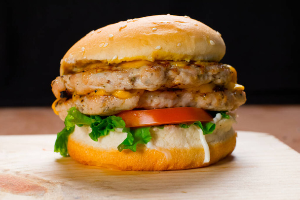 Primer plano en crujiente hamburguesa de pollo doble con lechuga y tomate. Sabrosa hamburguesa de pollo sobre fondo oscuro
. - Foto, Imagen