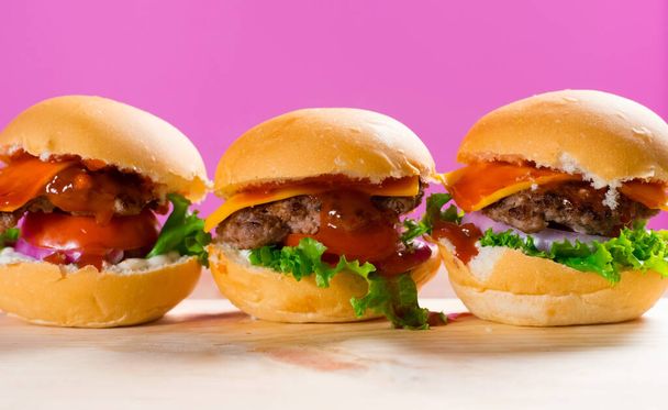Állítsa be a finom marhahús burger salátával paradicsom hagyma sajt fából készült asztal és rózsaszín háttér. Friss ízletes marhahús burger sajttal. - Fotó, kép