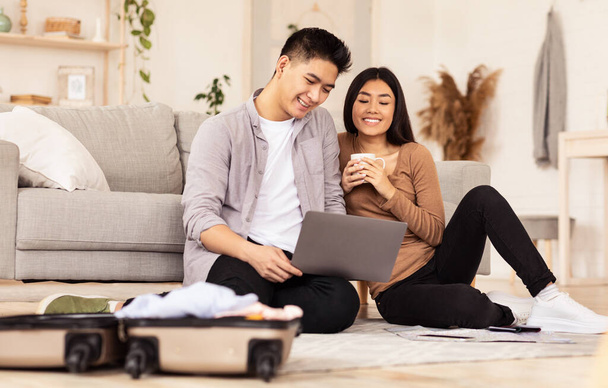 Azji para za pomocą laptopa siedzi w pobliżu rozpakowane walizki w domu - Zdjęcie, obraz