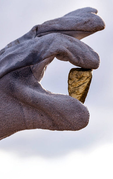 gold stone close-up in the hand of a mining company with glove. Mining exploration concept. - Photo, Image
