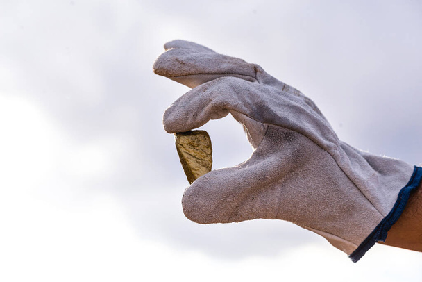 gold stone close-up in the hand of a mining company with glove. Mining exploration concept. - Photo, Image