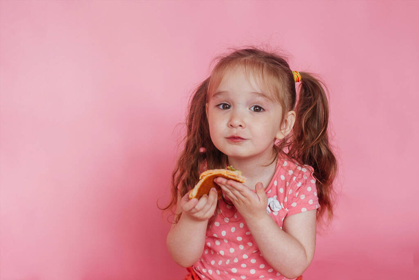 Beautiful little girl eating pizza. Pink background. Copy space - Фото, зображення