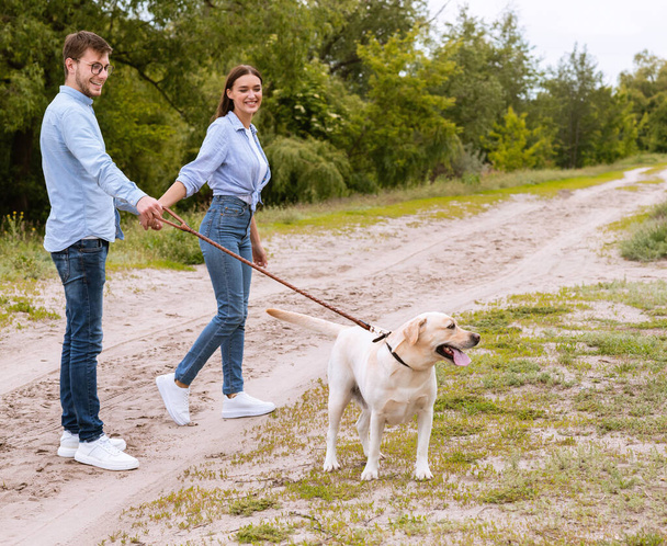 田舎を歩く若い夫婦とラブラドール - 写真・画像
