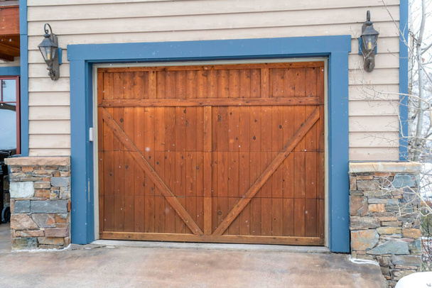 Porta garage in legno marrone con telaio blu affiancato da lanterne vintage montate a parete - Foto, immagini