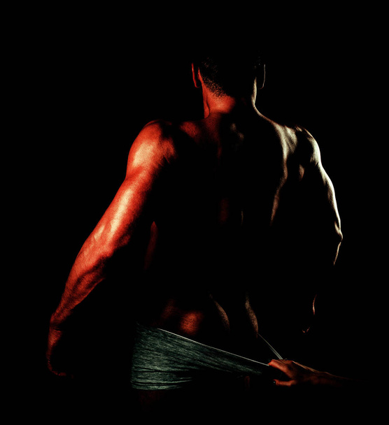 Female hand undresses pants. Fashion brutal guy with sexy naked torso. Muscular model man on dark background. Guy. Muscular man. - 写真・画像