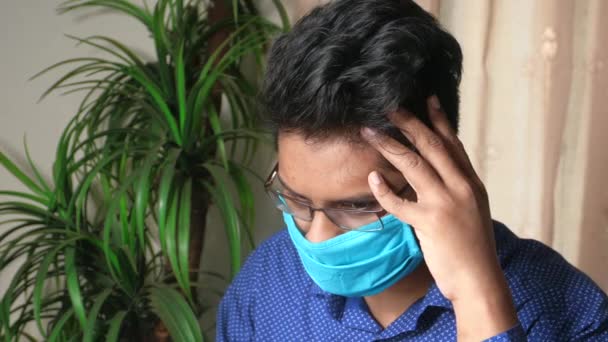 Μια νεαρή ασιατική μάσκα στο πρόσωπό του που υποφέρει από πονοκέφαλο.  - Πλάνα, βίντεο
