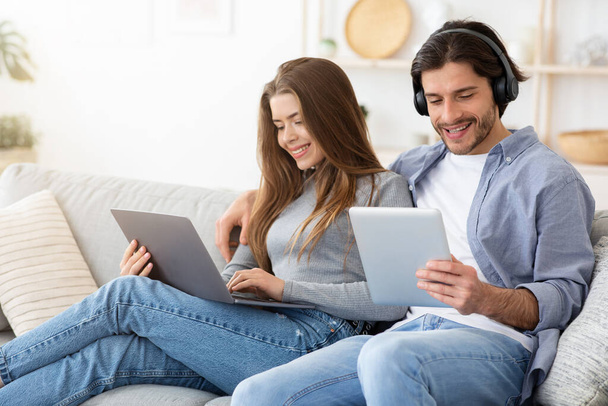 Lächelnder Mann und Frau mit elektronischen Geräten, Wohnbereich - Foto, Bild