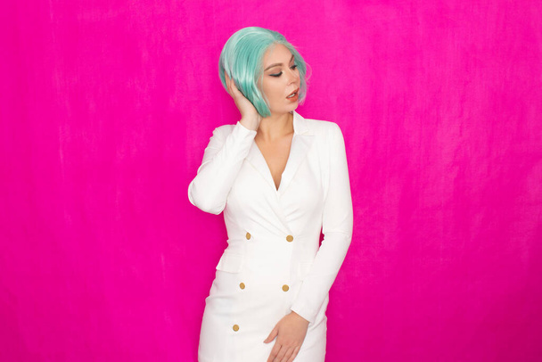 Beautiful young woman with short hair in menthol colors in a white business jacket dress posing against a fuchsia background in studio - Photo, image