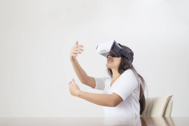 Mujer joven que actúa mientras usa dispositivos VR o gafas de realidad virtual sobre fondo blanco
. - Foto, imagen