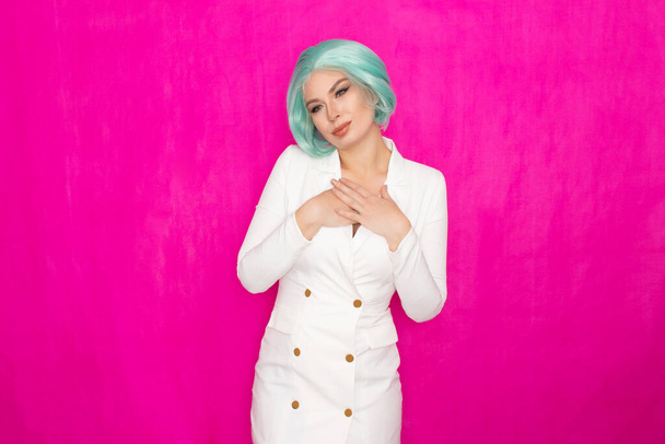 Beautiful young woman with short hair in menthol colors in a white business jacket dress posing against a fuchsia background in studio - Фото, изображение