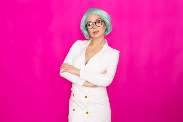 Beautiful young woman with short blue hair in glasses in a white business dress jacket posing on a bright pink background in the studio - Foto, afbeelding