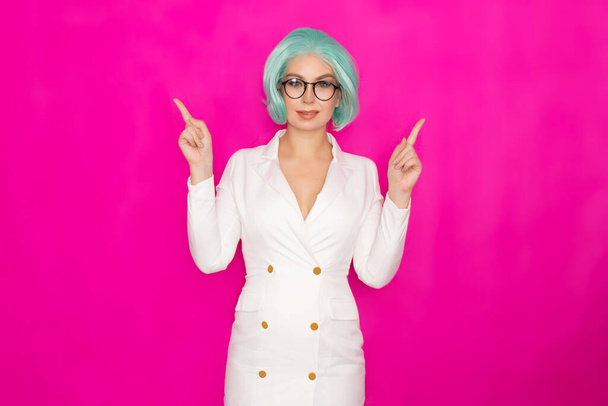 Beautiful young woman with short blue hair in glasses in a white business dress jacket posing on a bright pink background in the studio - Photo, image
