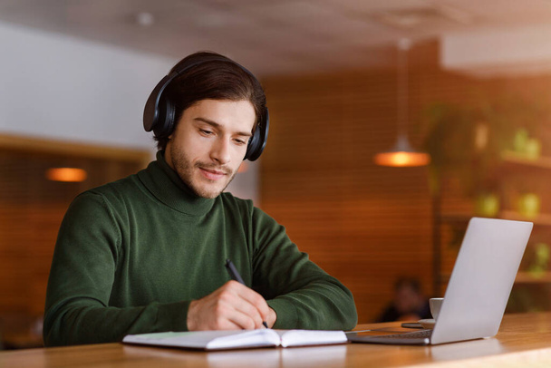 Skoncentrowany facet z słuchawkami studiuje online, za pomocą laptopa - Zdjęcie, obraz