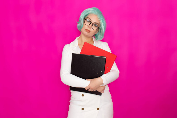 Beautiful young woman with short blue hair wearing glasses in a white business jacket dress holds two thick folders in her hands - Φωτογραφία, εικόνα