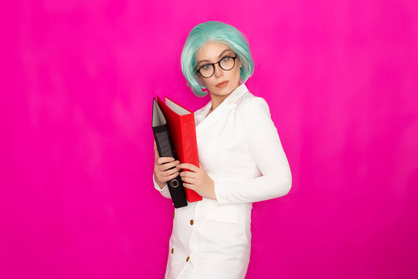 Beautiful young woman with short blue hair wearing glasses in a white business jacket dress holds two thick folders in her hands - Photo, image
