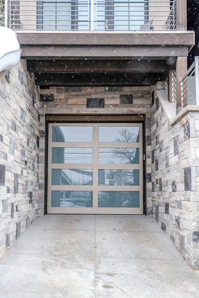 ガラスパネルガレージのドアと石の外壁で家に落ちる雪 - 写真・画像