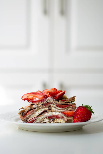 Ελαφρύ καλοκαιρινό επιδόρπιο: μια φέτα κέικ με σαντιγί, κομματάκια σοκολάτας και φράουλες ανάμεσα στις στρώσεις. Είναι διακοσμημένο με φράουλες και τοποθετείται σε λευκό πιάτο. - Φωτογραφία, εικόνα